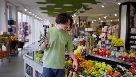 Un-Chico-Moreno-De-Pelo-Rizado-Escribe-Un-Blog-Sobre-Comida-En-Un-Supermercado-Y-Se-Graba-A-Sí-Mismo-Con-Una-Cámara-Usando-Un-Teléfono-Inteligente.