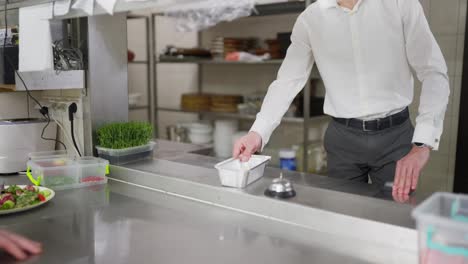 Un-Chef-Con-Uniforme-Negro-Pasa-El-Plato-Terminado-Al-Camarero-Para-Que-Lo-Empaque-Y-Lo-Entregue-Fuera-Del-Restaurante.-Empaquetado-De-Un-Plato-De-Restaurante-Para-Entrega-A-Domicilio