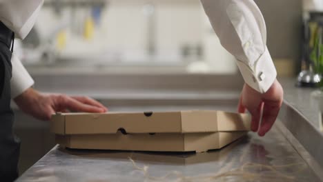 Cerca-De-Allí,-Un-Camarero-Con-Una-Camisa-Blanca-Larga-Coloca-La-Tarta-De-Queso-Terminada-En-Una-Caja-De-Cartón-Cuadrada-Y-La-Ata-Con-Una-Cuerda-Para-Enviarla-Al-Cliente.