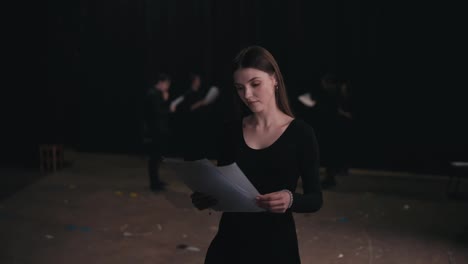 Portrait-of-a-confident-girl-actor-in-a-black-suit-who-revises-her-text-and-script-of-the-work-during-a-rehearsal-and-preparation-for-a-performance-on-stage-in-the-theater