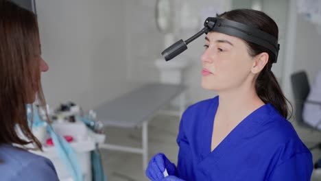 Over-the-shoulder-of-a-confident-brunette-girl.-An-ENT-doctor-in-a-blue-uniform-puts-a-wooden-stick-in-a-girls-mouth-to-check-for-throat-diseases-in-a-modern-clinic