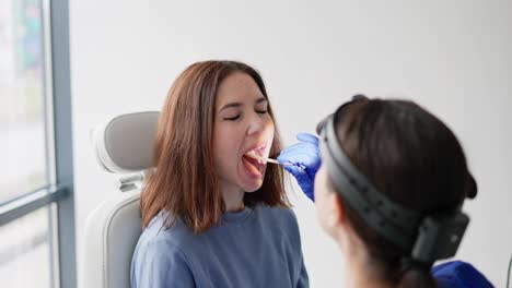 A-young-brunette-girl-at-an-appointment-with-an-ENT-specialist-closes-her-mouth-because-she-cannot-keep-it-open-for-a-long-time-while-studying-her-throat-in-the-ENT-office-in-a-modern-clinic