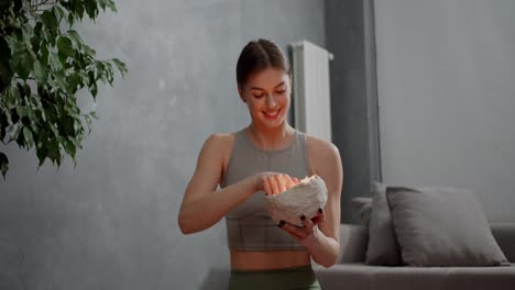 Happy-calm-brunette-girl-in-a-gray-top-and-green-sweatpants-lights-a-special-homemade-aromatic-candle-before-doing-yoga-and-sports-in-a-modern-apartment-at-home