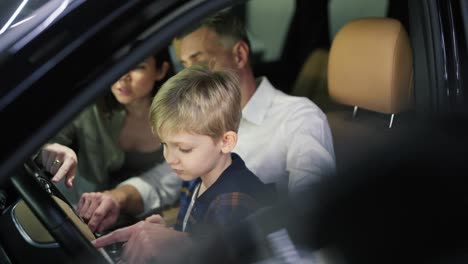 Close-up-of-a-little-blond-boy-in-a-plaid-shirt-sits-with-his-father-and-mother-in-the-interior-of-a-car-in-a-car-dealership