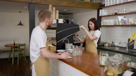 Happy-brunette-barista-girl-in-a-yellow-apron-communicates-with-a-male-waiter-during-a-working-day-in-a-cafe