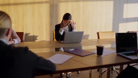 A-tired-girl-in-round-glasses-and-a-business-uniform-a-businesswoman,-sits-at-the-table-and-tries-to-relax-during-a-hard-day-at-work-with-her-colleagues