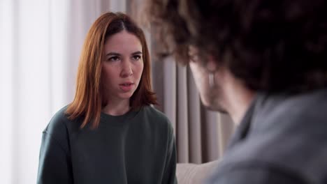 Over-the-shoulder-close-up-an-angry-brunette-girl-in-a-green-jacket-hits-her-boyfriend-on-the-cheek-with-her-palm-during-a-difficult-conversation-and-argument-about-life-and-relationships-at-home