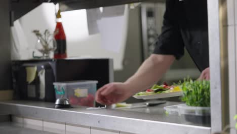 A-cook-in-a-black-uniform-puts-the-finished-salad-dish-on-the-serving-table-and-notifies-the-waiter-about-this-using-a-bell-in-a-restaurant