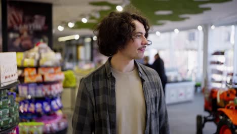 A-confident-brunette-guy-in-a-checkered-shirt-walks-through-a-grocery-store-and-examines-the-goods-on-the-shelves