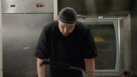 A-tired-sad-cook-in-a-black-uniform-takes-off-his-hat-during-a-hard-day-at-work-and-leans-his-elbows-on-the-table-trying-to-rest-during-a-hard-day-at-work-in-the-kitchen-of-a-restaurant