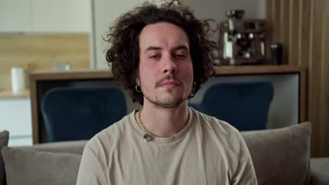 Portrait-of-a-sleepy-tired-brunette-guy-with-curly-hair-in-a-gray-T-shirt-who-is-falling-on-a-pillow-on-the-sofa-at-home