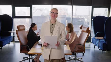 Portrait-Confident-middle-aged-businesswoman-with-glasses-in-a-white-suit-holding-a-sheet-of-paper-in-her-hands-while-working-in-the-office-Near-the-table