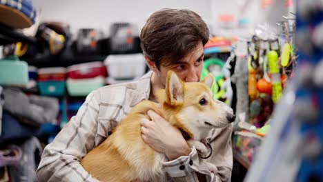 A-confident-brunette-guy-in-a-white-shirt-holds-a-red-corgi-dog-in-his-hands-and-chooses-food-for-it-in-a-pet-store