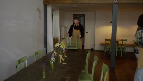 A-blond-man-in-a-yellow-apron-and-his-colleague-a-brunette-girl-place-chairs-on-the-table-while-cleaning-and-ending-the-day-in-a-cafe