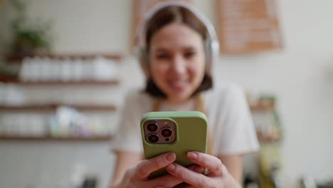 A-brunette-girl-holds-a-green-phone-in-her-hands-during-her-work-as-a-waiter-and-a-break-in-a-cafe