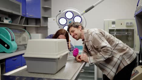 A-happy-brunette-guy-in-a-checkered-shirt-together-with-a-brunette-veterinarian-girl-takes-a-pet-out-of-a-carrier-in-a-veterinary-clinic