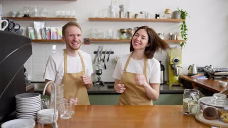 A-happy-brunette-waiter-girl-in-a-yellow-apron-dances-with-her-colleague-and-a-blond-guy-while-standing-at-the-counter-in-a-cafe