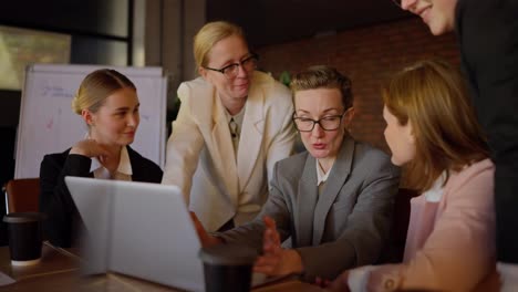 Middle-aged-girl-speaker-in-glasses-and-gray-uniform-presenting-her-work-during-a-meeting-of-businesswoman-colleagues-in-a-modern-office