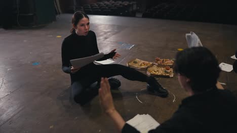 Zoom-in-confident-and-expressive-brunette-girl-actor-in-a-black-suit-sits-on-stage-in-the-theater-and-talks-with-another-actor-about-his-role-and-script