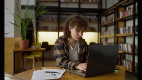 A-student-girl-with-curly-hair-does-a-warm-up-while-working-on-a-laptop-in-the-university-library