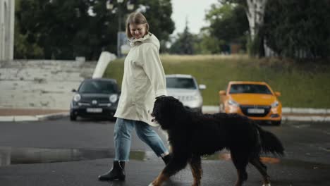 Happy-blonde-woman-in-a-white-jacket-walks-and-walks-with-her-big-black-dog-after-the-rain-in-the-park