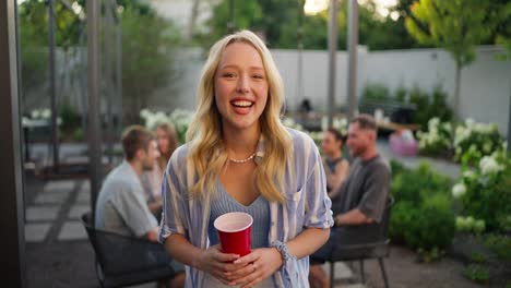 Retrato-De-Una-Chica-Rubia-Alegre-Y-Feliz-Con-Una-Camisa-Azul-Posando-Y-Riendo-Mientras-Se-Relaja-Con-Sus-Amigos-En-El-Patio-De-Una-Casa-De-Campo.