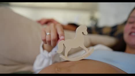 Zoom-Out-happy-brunette-woman-with-her-middle-aged-husband-playing-with-small-wooden-toy-while-expecting-baby-during-pregnancy-at-home