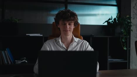 Portrait-of-a-happy-young-guy-with-curly-hair-working-at-a-laptop-posing-and-smiling-in-the-office