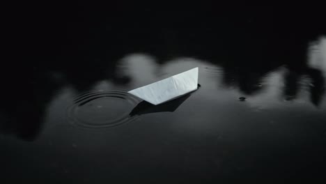 Close-up-a-white-paper-boat-floats-through-a-deep-puddle-after-rain-on-the-street