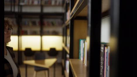 Happy-girl-student-with-curly-hair-wearing-glasses-puts-a-book-on-a-shelf-in-the-library