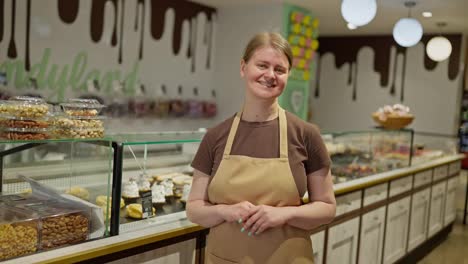 Porträt-Eines-Glücklichen-Mädchens-In-Einem-Braunen-T-Shirt-Und-Einer-Schürze,-Das-In-Der-Nähe-Einer-Konditorei-In-Einem-Supermarkt-Posiert.-Porträt-Eines-Glücklichen-Mädchens,-Das-Während-Seiner-Arbeitsschicht-In-Einer-Konditorei-In-Einem-Supermarkt-Arbeitet