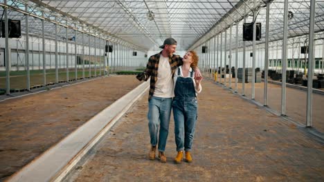 Happy-guy-in-a-plaid-shirt-walks-along-the-greenhouse-with-his-farmer-girlfriend-and-discuss-their-plans-to-work-in-the-greenhouse-on-the-farm