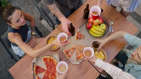 Top-view-of-a-happy-company-clinking-glasses-and-brown-bottles-together-during-the-start-of-a-party-at-a-table-in-the-courtyard-of-a-country-house