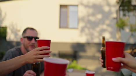 Close-up-a-group-of-young-friends-clink-glasses-together-at-a-table-during-lunch-in-the-courtyard-of-a-suburban-house