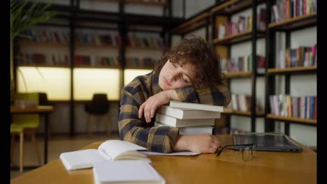 A-girl-with-curly-hair-in-a-plaid-shirt-lies-on-a-stack-of-books-at-the-table-and-sleeps-in-the-library