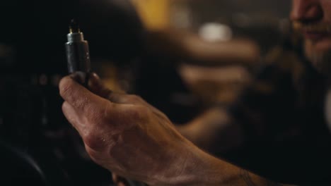 Close-up-of-a-guy-mechanic-inspecting-a-spark-plug-while-repairing-a-motorcycle-and-picking-up-tools-in-his-workshop-studio