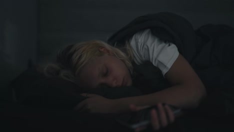 A-blonde-girl-in-a-white-T-shirt-wakes-up-abruptly-and-looks-anxiously-at-the-phone-at-night