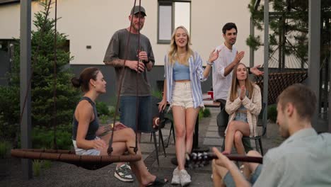 Un-Alegre-Grupo-De-Amigos-Canta-Una-Canción-Mientras-Su-Amigo-Toca-Una-Alegre-Melodía-En-La-Guitarra-Durante-Una-Fiesta-En-El-Patio-Trasero-De-Una-Casa.