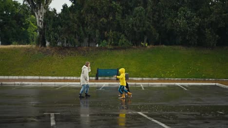 Happy-teenage-girl-running-around-her-mom-in-a-white-jacket-along-with-her-black-dog-while-walking-in-the-rain-in-the-park