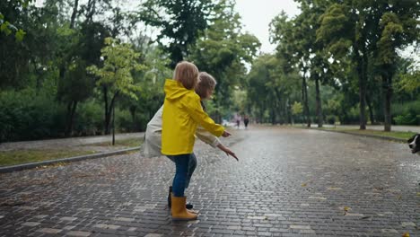 A-happy-girl-in-a-yellow-jacket-and-her-mother-pet-a-large-black-dog-while-walking-on-an-alley-in-the-park-after-the-rain