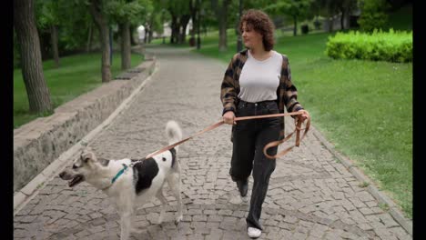 Happy-brunette-girl-with-curly-hair-walks-with-her-white-dog-in-the-park.-Walk-with-your-pet-during-the-day