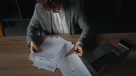 Close-up-a-confident-young-guy-in-a-gray-suit-examining-documents-and-work-reports-sitting-at-a-table-in-the-office