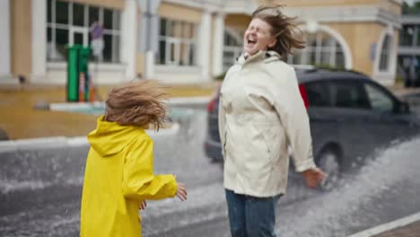 Ein-Vorbeifahrendes-Auto-Schüttet-Wasser-Aus-Einer-Pfütze-Auf-Eine-Blonde-Frau-In-Einer-Weißen-Jacke-Und-Ihre-Teenager-Tochter,-Während-Sie-Im-Park-Spazieren-Gehen