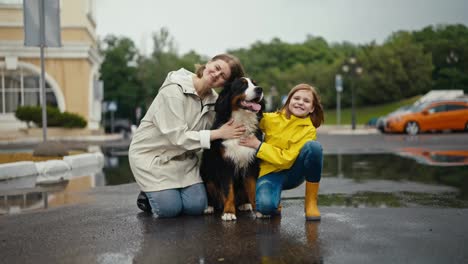 Porträt-Einer-Glücklichen-Blonden-Frau,-Die-Mit-Ihrer-Tochter-Im-Teenageralter-Und-Einem-Schwarzen-Hund-Beim-Spaziergang-Im-Park-Nach-Dem-Regen-Sitzt