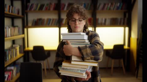 Portrait-of-a-brunette-student-girl-in-glasses-who-carries-a-stack-of-books-near-the-shelves-in-the-library