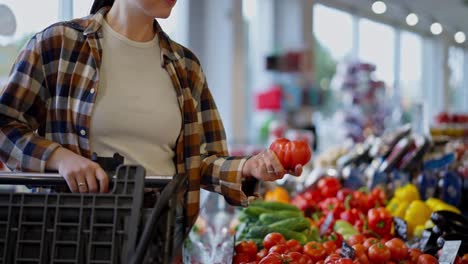 Close-up-a-brunette-girl-in-a-checkered-shirt-brings-tomatoes-to-her-nose-and-tastes-the-aroma-of-a-ripe-vegetable-while-shopping-in-a-supermarket