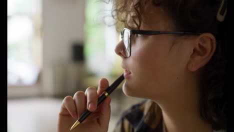 A-pensive-brunette-girl-with-curly-hair-and-glasses-takes-notes-while-she-studies-and-does-homework-in-the-university-library