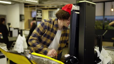 Happy-food-delivery-guy-in-a-plaid-shirt-punches-the-necessary-products-and-then-puts-them-in-his-yellow-bag-for-food-delivery-in-the-supermarket