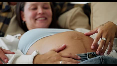 Close-up-of-a-happy-brunette-woman-with-her-husband-stroking-her-pregnant-belly-during-her-pregnancy-at-home-in-a-modern-apartment