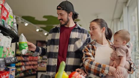 A-confident-brunette-woman-in-a-checkered-shirt-advises-what-to-choose-for-her-husband-during-family-shopping-with-a-small-child-in-the-supermarket